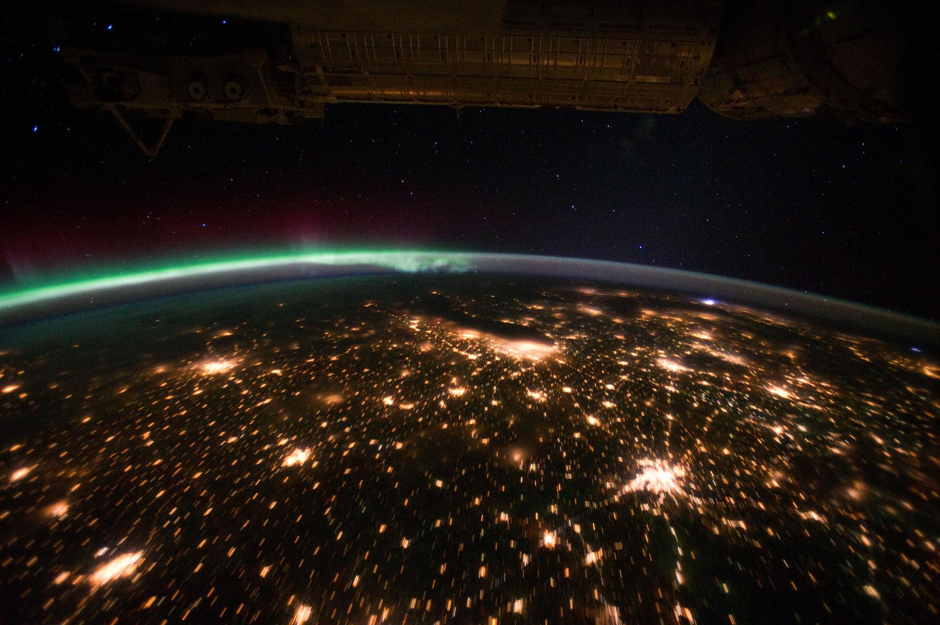 Aurora borealis with city lights on the horizon, taken from the ISS